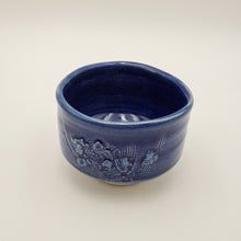 A small ceramic bowl with a glossy cobalt blue glaze and embossed floral details on the exterior, set against a plain light background.