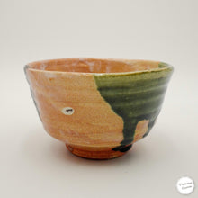 A handmade ceramic bowl with a natural terracotta base and a glossy dark green glaze dripping down the right side, shown on a neutral light gray background.