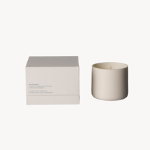 A minimalist cream-colored ceramic candle in a matching cylindrical holder, displayed next to its textured cream packaging box on a clean white background.