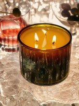 Lit candle in glass holders on a reflective surface with a blurred background
