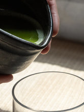 Person holding a bowl of green tea over a glass on a textured surface
