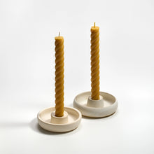Two twisted beeswax candles in ceramic holders on a white background
