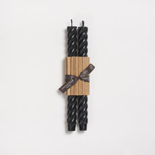 Two black twisted candles wrapped with brown paper and a ribbon on a white background