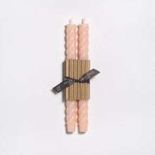 Two pink candles with a ribbed texture are wrapped together with a black ribbon on a light gray background.
