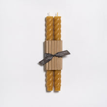 Two twisted beeswax candles wrapped in paper with a ribbon on a white background