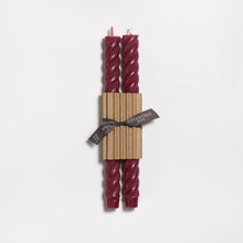 Twisted red candles in cardboard packaging with a tag on a white background