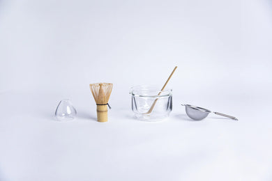 Tea-making tools including a whisk, glass bowl, and strainer on a white background