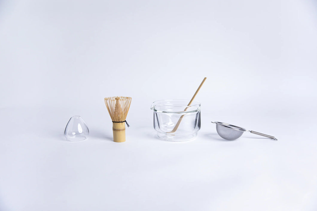 Tea-making tools including a whisk, glass bowl, and strainer on a white background