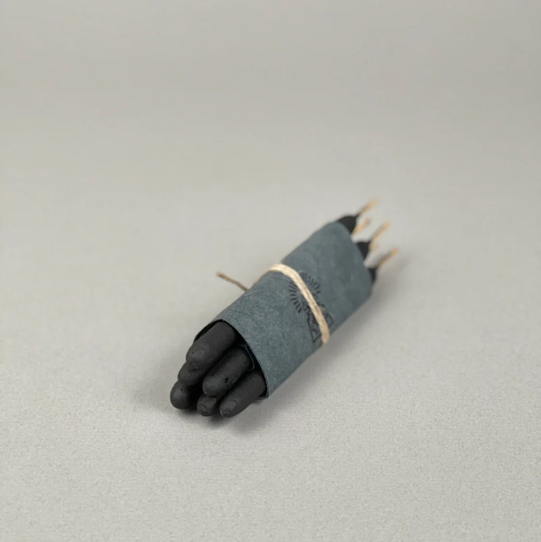 Black incense wrapped in gray paper on a light gray background