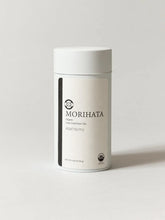 A white cylindrical canister of Morihata Asatsuyu green tea on a light gray background.