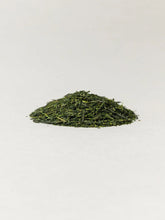 A small mound of loose-leaf green tea leaves centered on a plain white background.