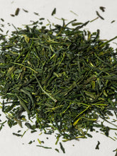 A pile of loose-leaf green tea leaves, showing various shades of green and yellow-green, scattered on a plain white surface.