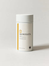 A white cylindrical canister of Morihata Genmaicha loose leaf green tea, featuring a minimalist cream label with a vertical gold stripe and black text, set against a clean light gray background.