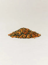 A small mound of roasted brown rice with green leaves, photographed on a clean off-white background.