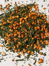 A close-up pile of roasted rice mixed with green tea leaves, scattered on a white surface.