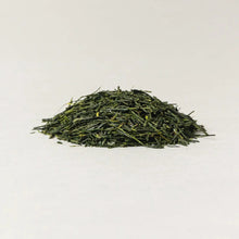 A small mound of loose-leaf green tea leaves on a plain white background.