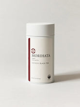 A white cylindrical canister of MORIHATA Organic black Tea (Hayashi) on a light gray background.