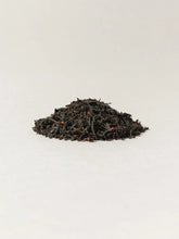 A small mound of dark loose-leaf tea with a few small orange-red accents, centered on a plain light background.