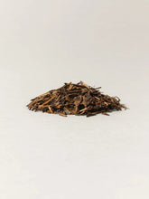 A small pile of loose-leaf tea brown leaves, photographed on a plain light background.