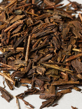 Close-up of loose, dried tea leaves dark brown and tan tones, scattered on a light neutral background.