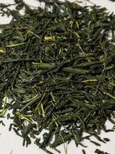 Close-up of loose-leaf green tea leaves scattered on a white surface.