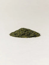 A small mound of loose-leaf green tea leaves centered on a plain light background.