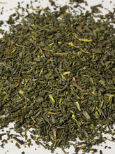 A close-up pile of loose-leaf tea leaves, primarily dark green with lighter yellow-green and olive highlights, scattered on a plain white background.