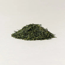 A small mound of loose-leaf green tea leaves on a plain white background.