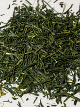 A close-up pile of loose-leaf green tea leaves on a plain white background.