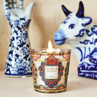 Decorative candle with intricate design in front of ceramic cow and hand figurines.