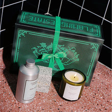 Gift set with a candle, bottle, and box on a textured surface with a black tiled background