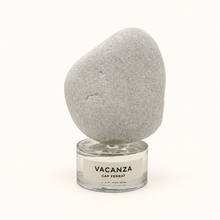 A gray decorative stone perfume cap, displayed on a clear glass jar candle with a white label reading 'VACANZA CAP FERRAT', set against a plain white background.
