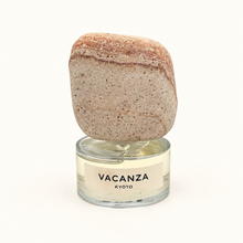 A perfume bottle with a clear glass base labeled 'VACANZA KYOTO' and a natural stone cap on a white background.