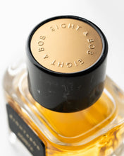 Close-up of a perfume bottle with a black cap and gold text on a white background