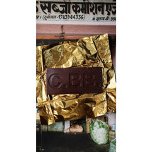 Chocolate bar with 'C.B.B.' branding wrapped in gold foil, with a blurred background.