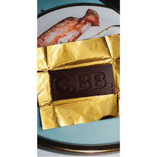 Chocolate bar with gold foil and 'CBB' branding on a white plate with fish.