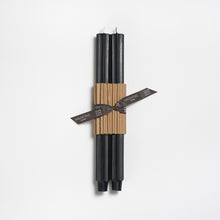 Set of black candles wrapped in brown paper with a label on a white background