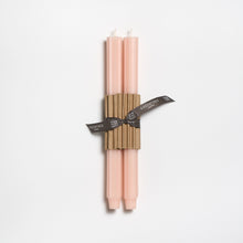 Two blush color candles tied with a brown ribbon on a white background