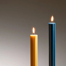 Two lit candles, one yellow and one blue, on a gray background