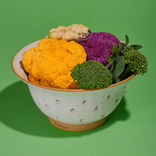 Colander filled with colorful cauliflower and broccoli on a green background