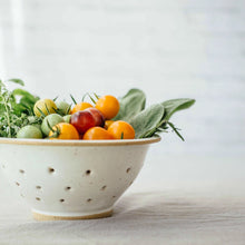 Colander with fruits and vegetables on a light surface