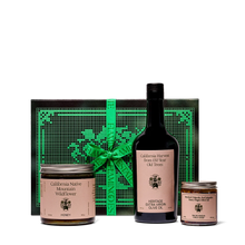 A curated gift set featuring a bottle of Heritage Extra Virgin Olive Oil, a jar of California Native Mountain Wildflower Honey, and a jar of Heritage Organic Salsa Macha, arranged in front of a decorative black and green gift box on a white background.