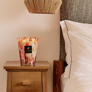 Candle on a wooden nightstand next to a bed with white pillows.