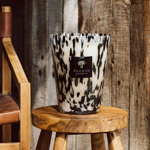 Decorative candle vessel with a leopard print pattern on a wooden stool against a rustic wooden wall.