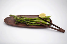 Oval walnut pebble tray with asparagus and lemon slice. Wood tong on the side