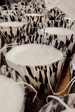 Hand poured candle with black and white patterned rims on a wooden surface