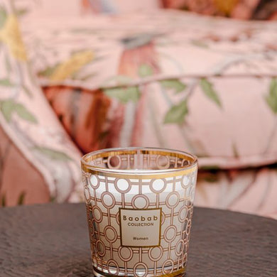 Decorative candle with 'Baobab Collection' on a table with a floral-patterned cushion in the background