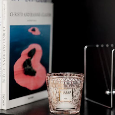 Candle in a decorative glass holder next to a book titled 'Christo and Jeanne-Claude' on a dark surface.