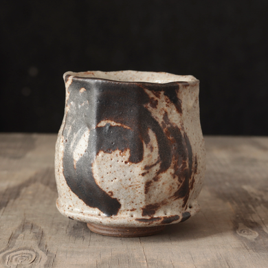 Ceramic cup with black and brown glaze on a wooden surface