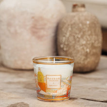 Candle in a decorative glass container on a wooden surface with ceramic jars in the background